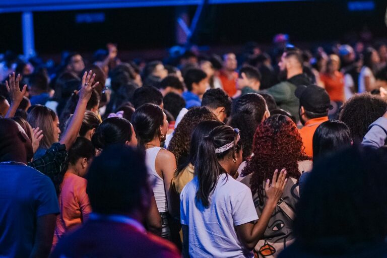 Back view of a large congregation standing in worship, raising hands in unity and spirituality.
